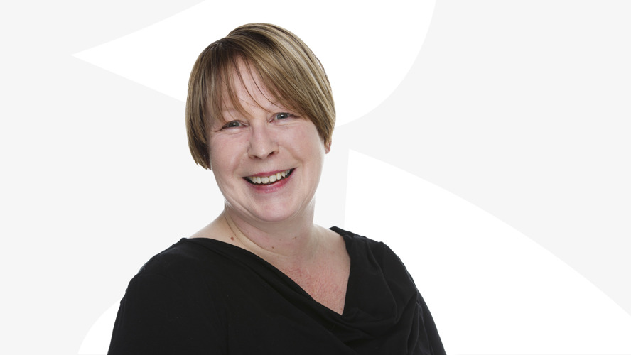 Anita Van Gils hymyilee valkoista taustaa vasten.