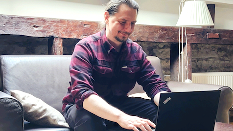 Mies istuu sohvalla ja kirjoittaa kannettavalla tietokoneella.