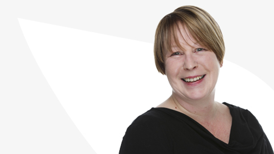 Anita Van Gils hymyilee valkoista taustaa vasten.