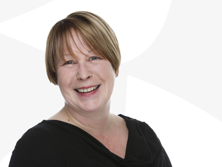 Anita Van Gils hymyilee valkoista taustaa vasten.