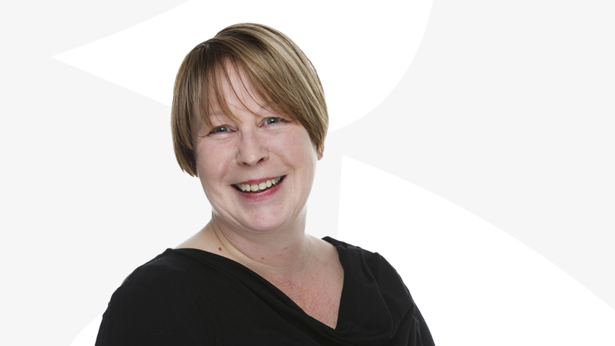 Anita Van Gils hymyilee valkoista taustaa vasten.