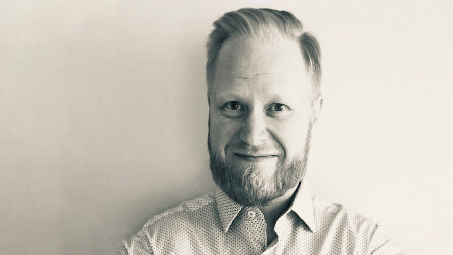 Parrakas Petteri hymyilee vaaleaa taustaa vasten.