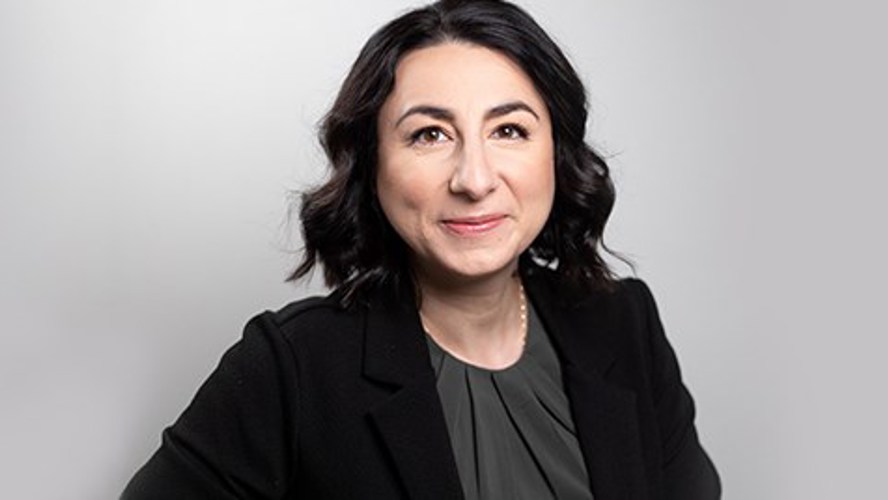 Tatjana katsoo kameraan hymyillen harmaata taustaa vasten.