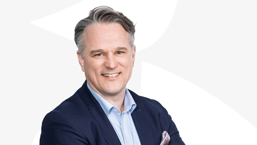 Toimitusjohtaja Janne Vainio katsoo hymyillen kameraan vaaleaa taustaa vasten.